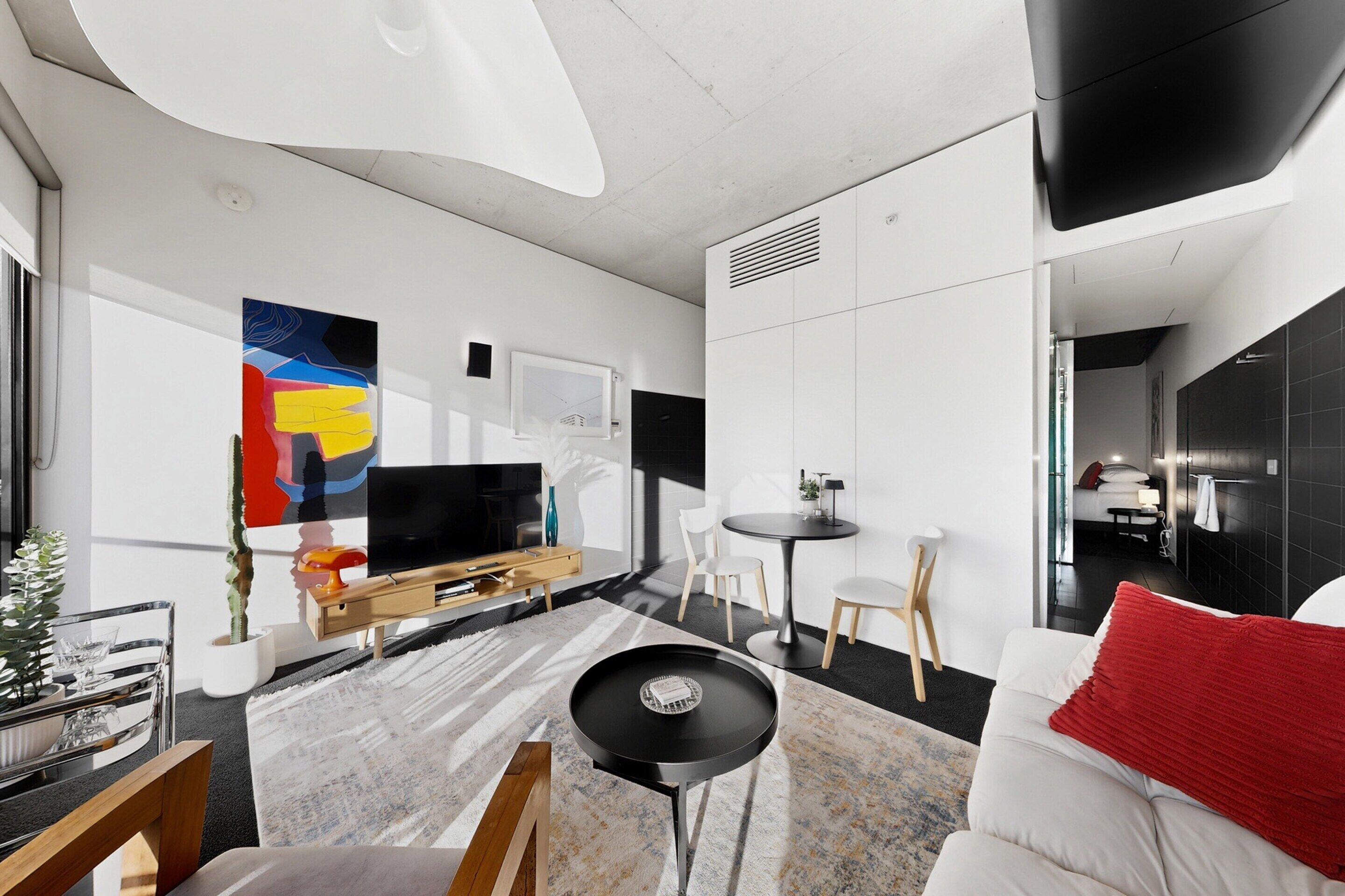 Un salon moderne avec un téléviseur à écran plat, une table basse et un canapé agrémenté d’un coussin rouge.