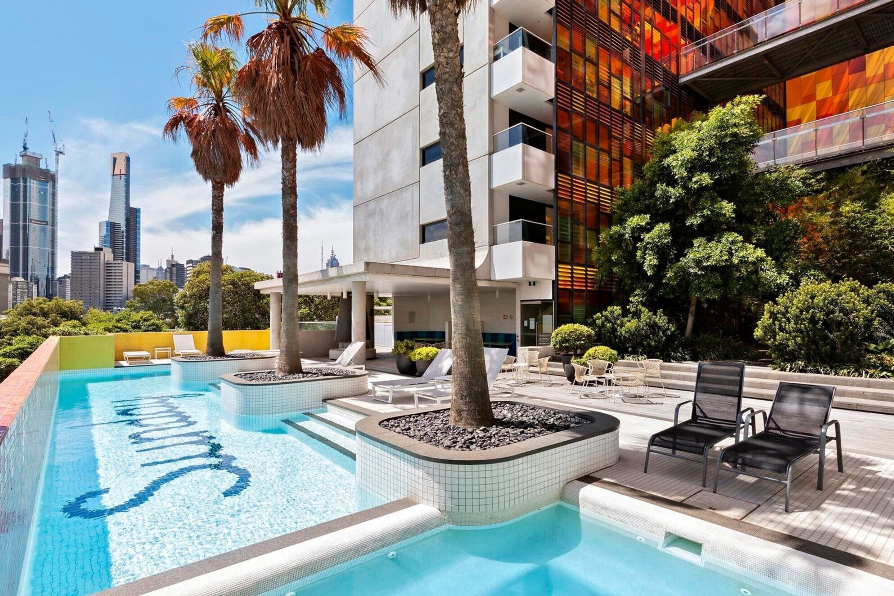 A modern building with a rooftop pool, lounge chairs, and a city skyline in the background.