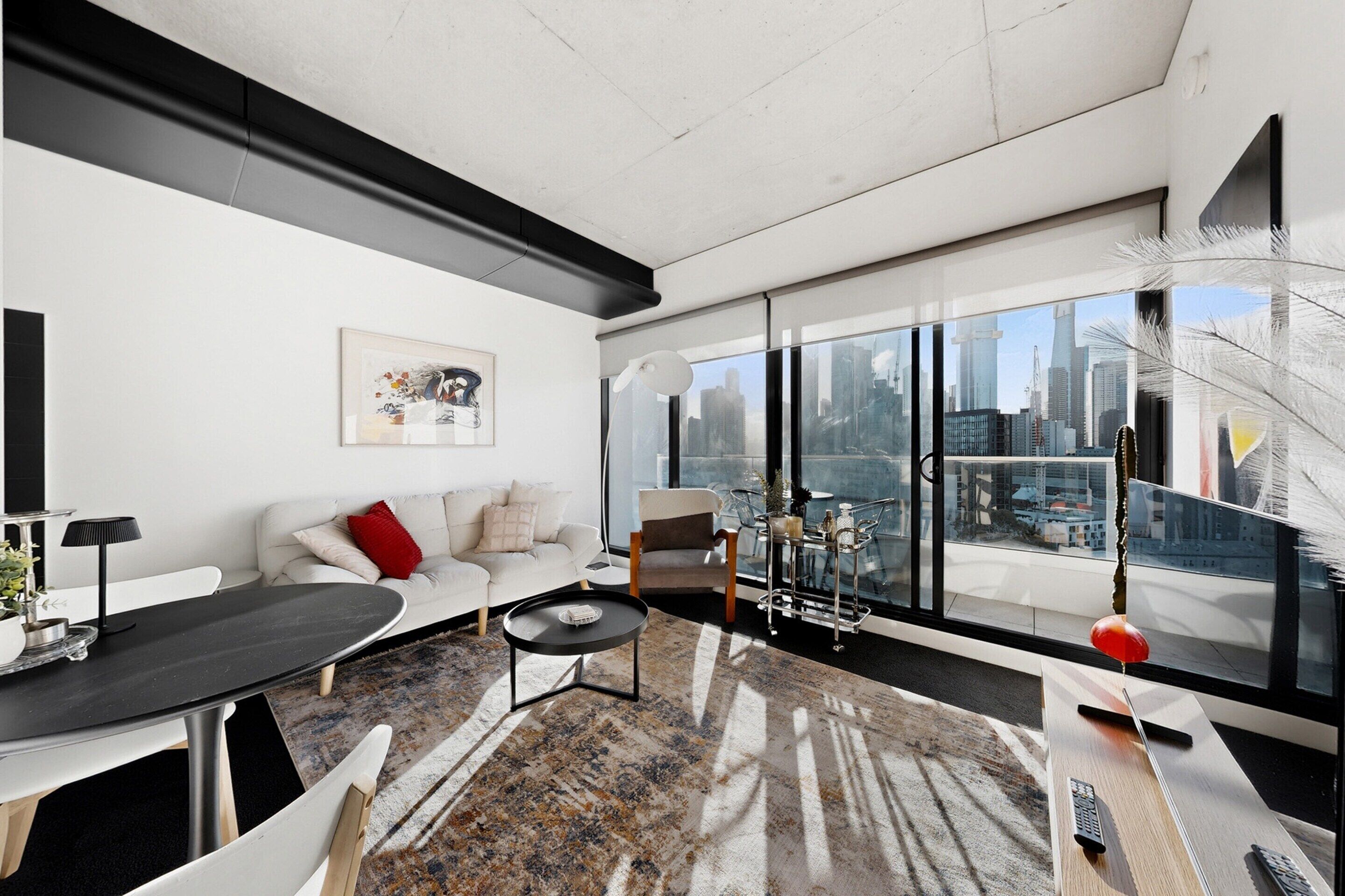 A modern living room with a sofa, a dining table, and a large window with a city view.