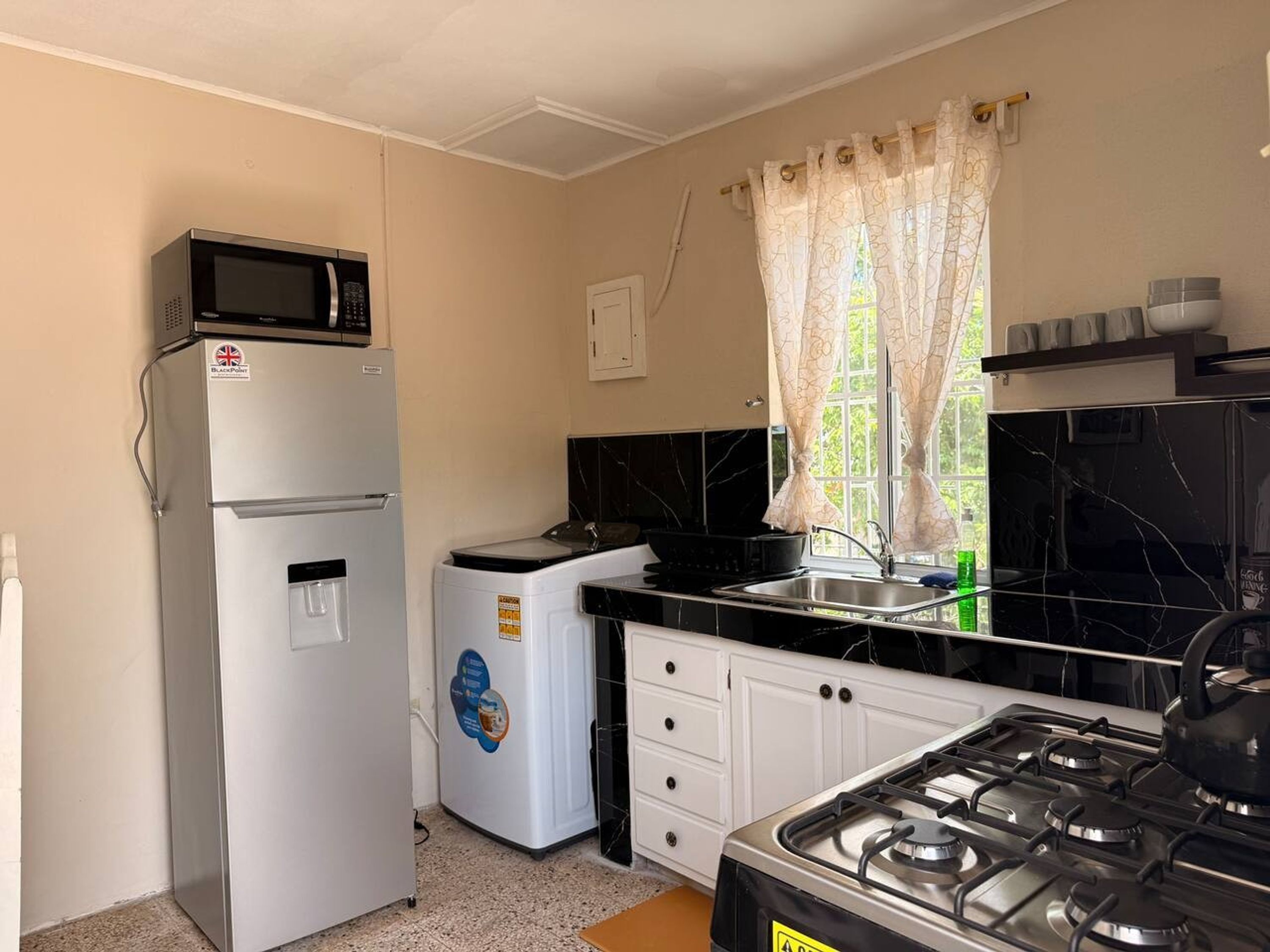 Een kleine keuken met een koelkast, een wasmachine, een fornuis en een raam met gordijnen.