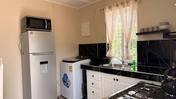 Een kleine keuken met een koelkast, een wasmachine, een fornuis en een raam met gordijnen.