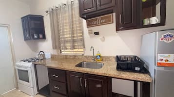 A kitchen with dark wooden cabinets, a granite countertop, a stainless steel sink, a gas stove, and a refrigerator with a logo.