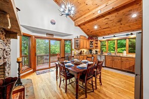 Une cuisine spacieuse avec des meubles en bois, un coin repas comprenant une table et des chaises en bois, et de grandes fenêtres offrant une vue sur l’extérieur.