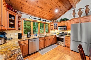 A modern kitchen with wooden cabinets, stainless steel appliances, and a large window overlooking greenery. - Sleeps 15!|Indoor Fireplace|HotTub|Pets OK|Game RM (Beech Mountain)
