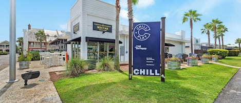 Un edificio moderno con un letrero de Nectar Coffee & Wine, un letrero de Chill Play y un césped bien cuidado con palmeras.
