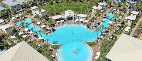 Una gran piscina circular rodeada de palmeras y sillas de descanso, con varios edificios al fondo.