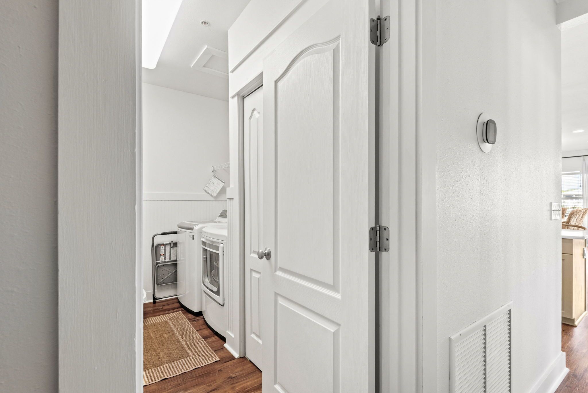 Un pasillo con una puerta blanca, un calentador integrado y vistas hacia una zona de cocina con lavadora.