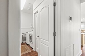 A hallway with a white door, a built-in heater, and a view into a kitchen area with a washing machine. - 4BR in Seacrest Beach w 4 Bikes & Lagoon Pool Views + Attraction Tickets! (Panama City Beach)
