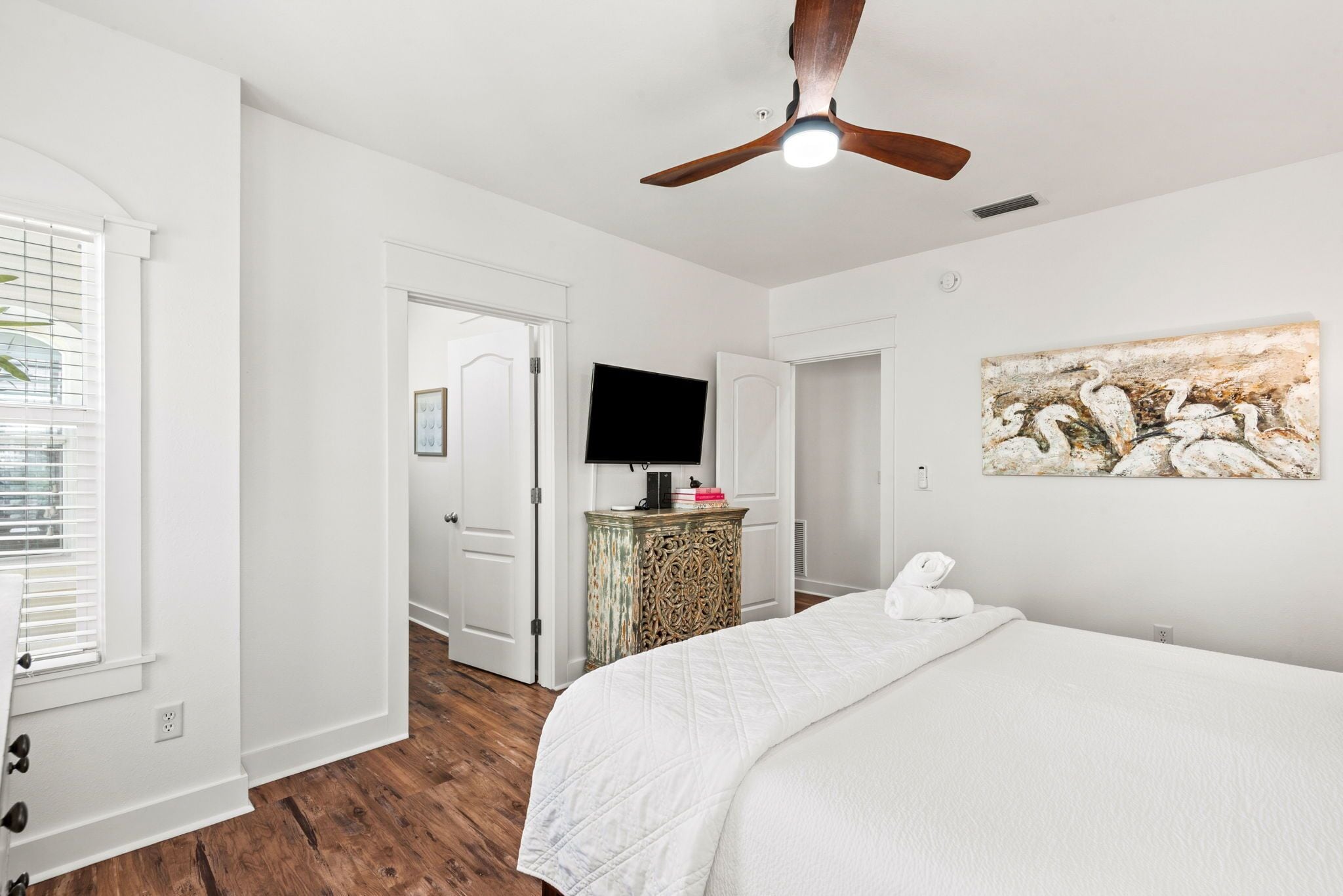 A bedroom with a bed, a ceiling fan, a television, and a painting on the wall.