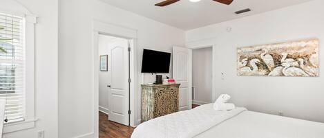 A bedroom with a bed, a ceiling fan, a television, and a painting on the wall.