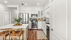 Una cocina moderna con armarios blancos, electrodomésticos de acero inoxidable y una mesa de comedor de madera con sillas.