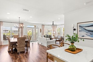 A spacious living area with a dining table, wicker chairs, a sofa, and a large window with blinds. - 4BR in Seacrest Beach w 4 Bikes & Lagoon Pool Views + Attraction Tickets! (Panama City Beach)