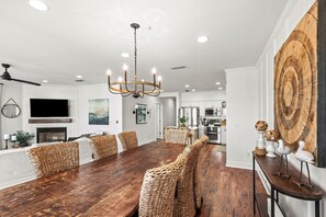 A spacious dining area with a long wooden table and wicker chairs, a modern kitchen with stainless steel appliances, and a large wooden wall art piece. - 4BR in Seacrest Beach w 4 Bikes & Lagoon Pool Views + Attraction Tickets! (Panama City Beach)