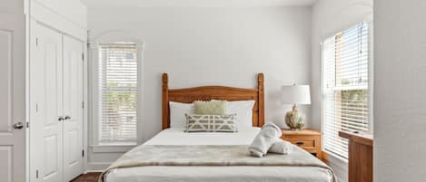 Une chambre à coucher comprenant un lit, un ventilateur de plafond, une table de chevet avec une lampe et une fenêtre avec des stores.