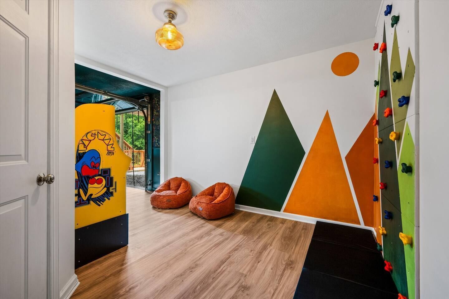 Una habitación con piso de madera, una pared de escalada y dos sillones de pelota.