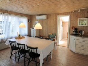 Ein Zimmer mit Holzwänden, einem Esstisch, Stühlen, einer Küchenzeile und einer Uhr an der Wand.