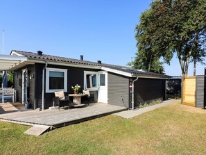 Ein eingeschossiges Haus mit überdachter Terrasse, einer kleinen Außen-Sitzgelegenheit und einer sichtbaren Garagentür.