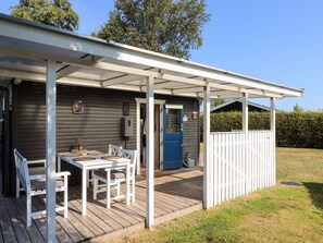A covered outdoor seating area with a table and chairs, a door, and a small shed in the background. - 8 Person Holiday Home in Hadsund (Hadsund)