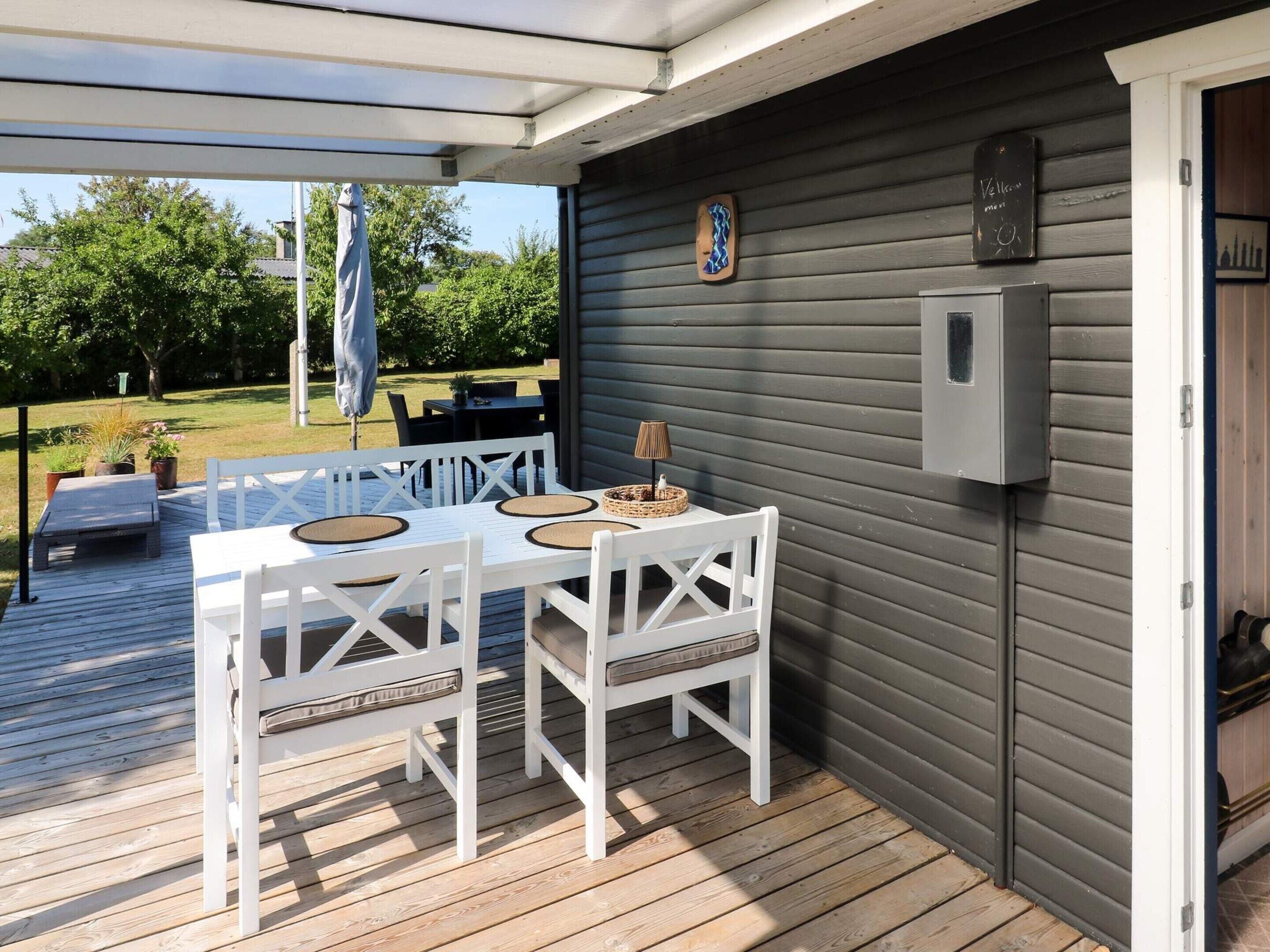 A covered outdoor patio with a table and chairs, a small wall-mounted electrical box, and a view of the backyard.