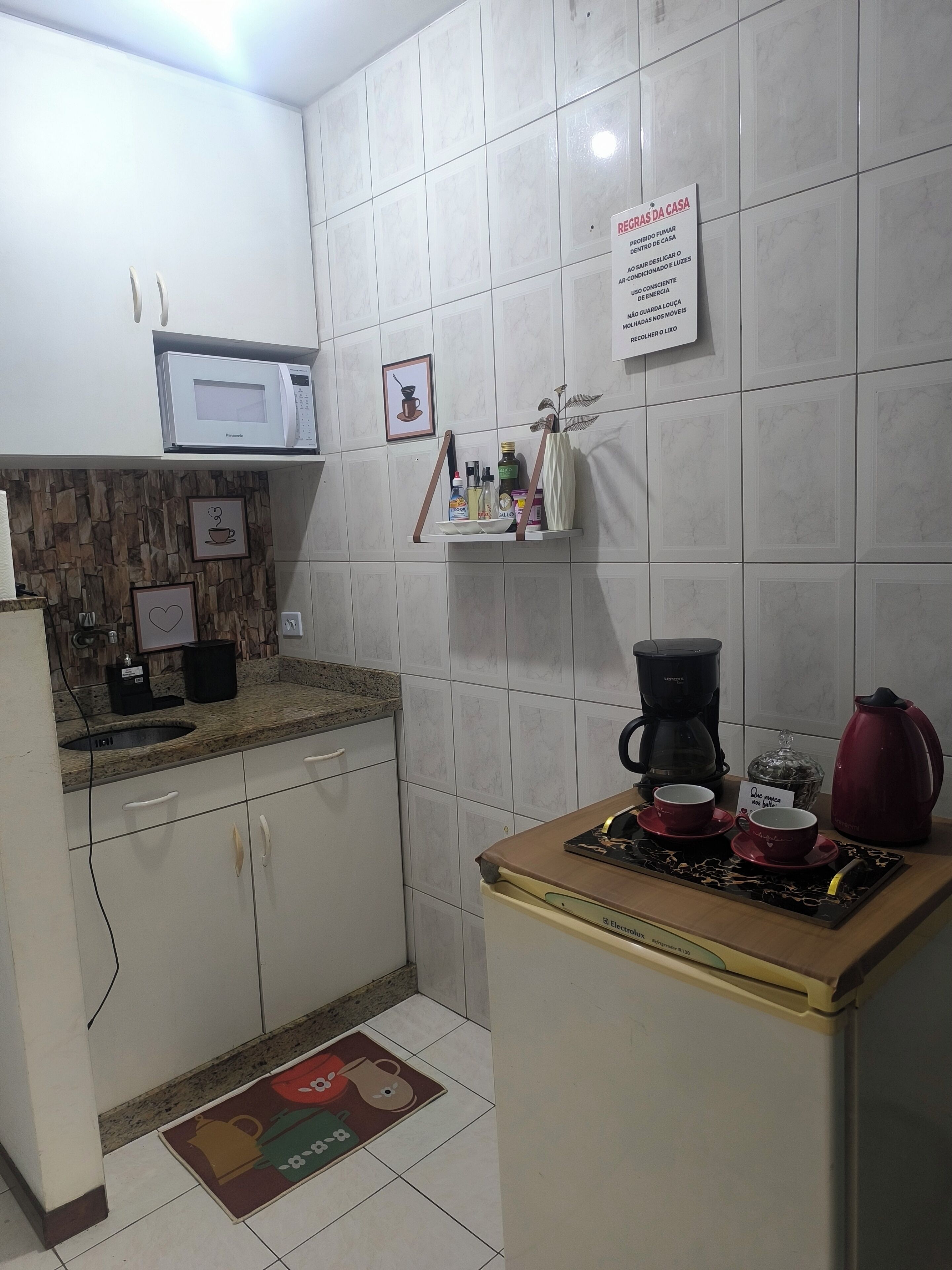 A kitchen with white tiled walls, a microwave, a coffee maker, and a red kettle.