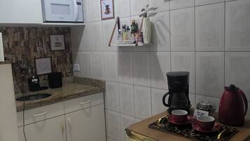 A kitchen with white tiled walls, a microwave, a coffee maker, and a red kettle.