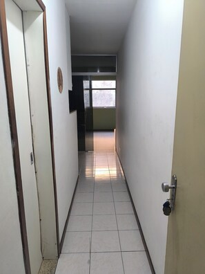A narrow hallway with tiled flooring, a door on the left, and a window at the end.