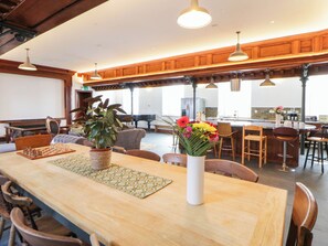 A spacious room with a long wooden table, multiple chairs, a chessboard, and a vase of flowers.