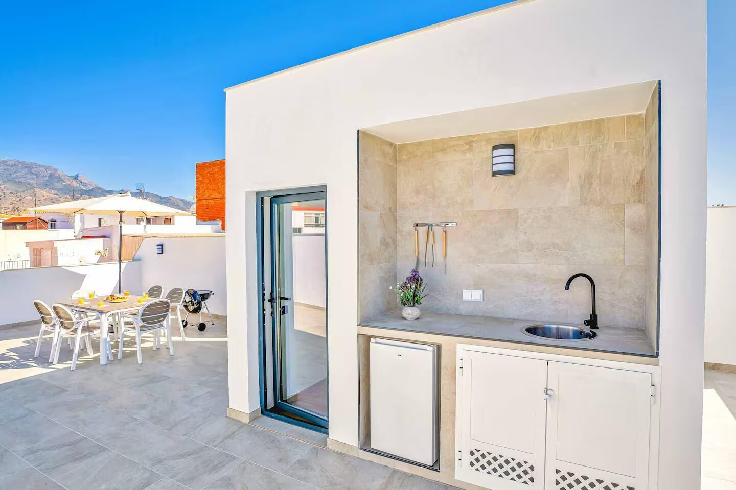 A compact outdoor kitchen with a sink and a dining area with chairs and a table.