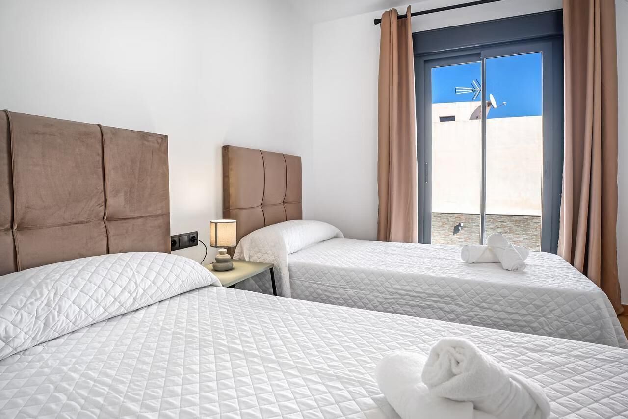 Une chambre d’hôtel avec deux lits, une table de chevet, une lampe et une vue sur la plage, visible à travers une grande fenêtre.