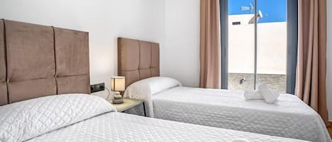 Une chambre d’hôtel avec deux lits, une table de chevet, une lampe et une vue sur la plage, visible à travers une grande fenêtre.