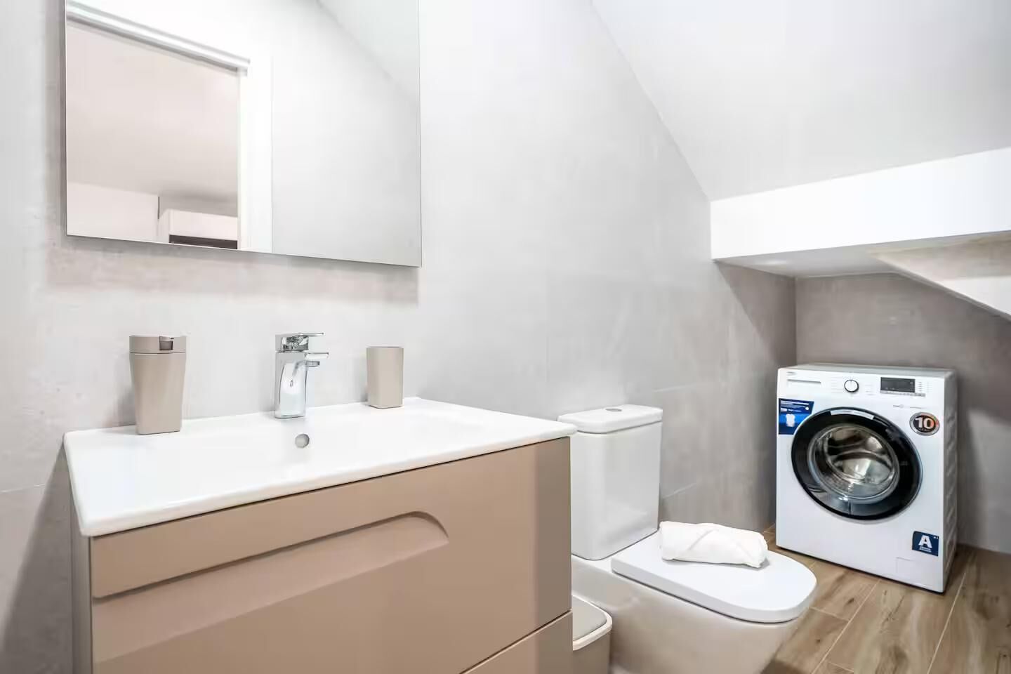 A modern bathroom with a white sink, mirror, and a washing machine.