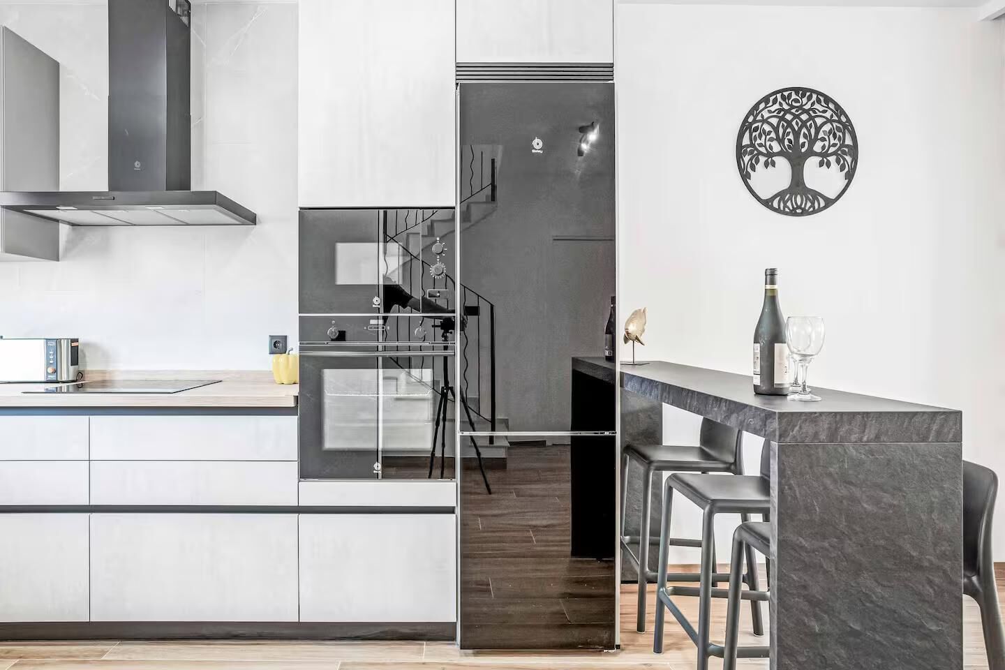 A modern kitchen with a built-in oven, a stainless steel range hood, and a glass-fronted refrigerator.