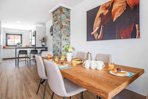 Ein moderner Essbereich mit einem Holztisch, gedeckt für das Frühstück, einer Küche im Hintergrund und einem großen Elefantenbild an der Wand.
