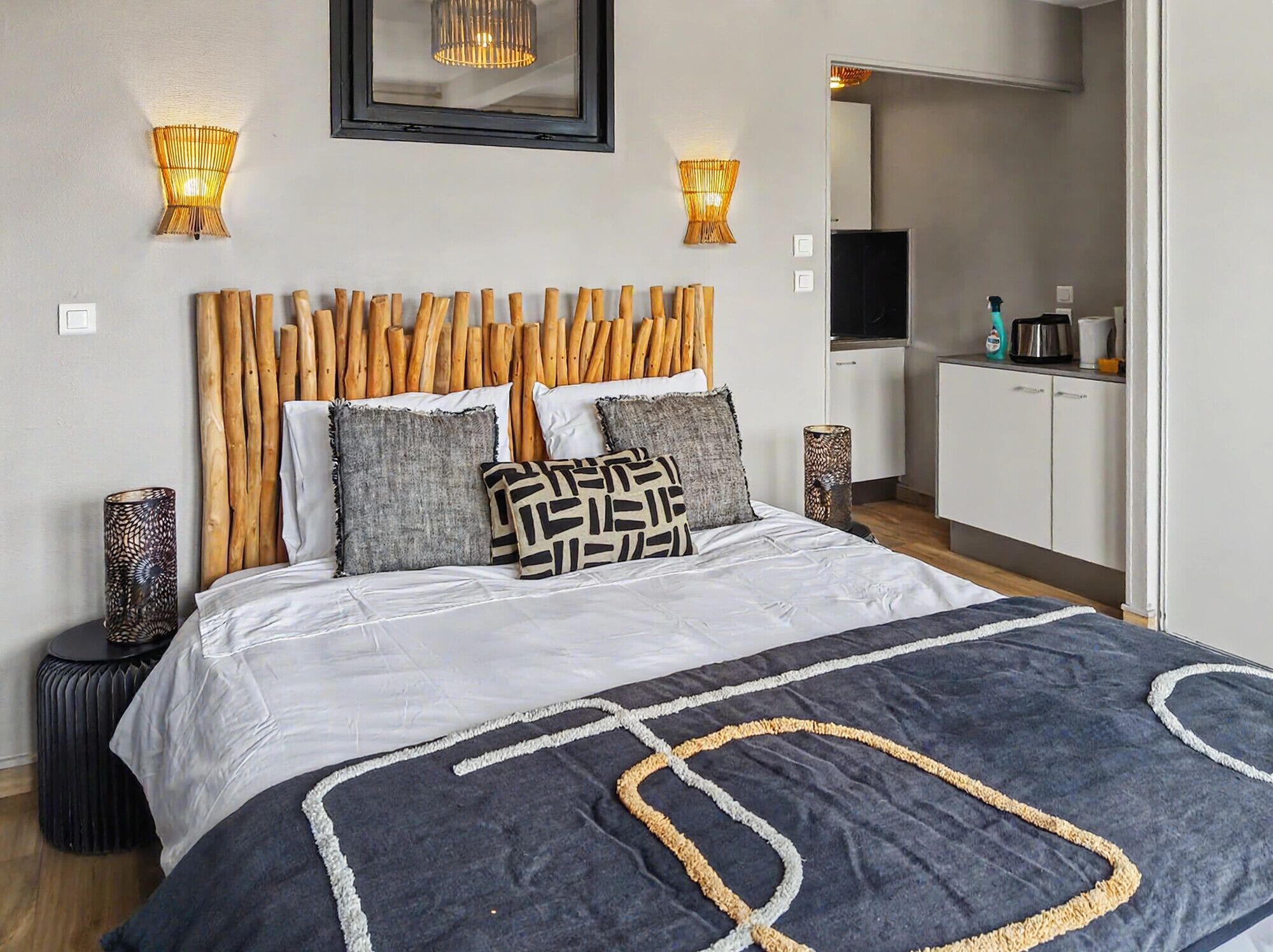 A bedroom with a wooden headboard, a bed with patterned pillows, and two wall-mounted lamps.