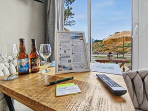 A wooden table with a welcome sign, wine bottles, glasses, a remote control, and a pen. - Cozy studio for 2 people — Les Villas de la Plage, Rospico (Névez) (Névez)