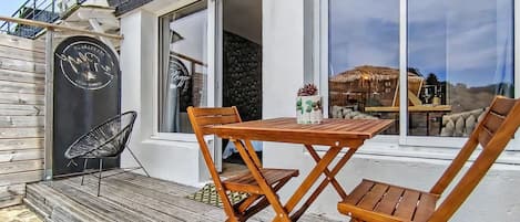 Eine Holzterrasse mit Tisch und Stühlen, ein schwarzer Sessel und eine Tür mit einem Logo.