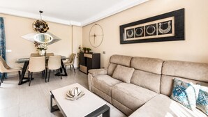 En moderne stue med sofa, sofabord, spiseområde med stole og et billede på væggen.
