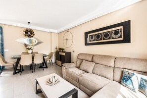Ein modernes Wohnzimmer mit Sofa, Couchtisch, Essbereich mit Stühlen und einem Wandbild.