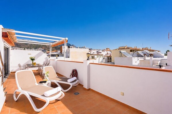A rooftop terrace with sun loungers, a table with chairs, and a view of the cityscape. - Villa Gloria - Four Bedroom Villa, Sleeps 6 (Nerja)