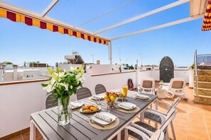 Eine Dachterrasse mit Esstisch, Stühlen, einem Blumenstrauß und Blick auf die Stadtlandschaft.