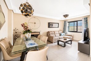 A modern living room with a glass dining table, beige sofas, and a TV on a stand. - Villa Gloria - Four Bedroom Villa, Sleeps 6 (Nerja)