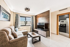 Uma sala de estar moderna com sofá, televisão e área de cozinha com eletrodomésticos.