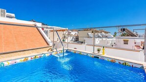 En pool på taget med en klar blå himmel, fliseterrasse og stålrækv.