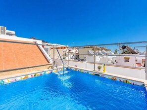 Ein Pool auf dem Dach mit blauem Himmel, einer gefliesten Terrasse und einem Metallgeländer.