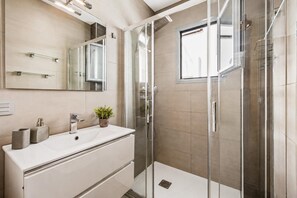 Ein modernes Badezimmer mit einer gläsernen Dusche, einem weißen Waschtisch mit Spiegel und einer Topfpflanze.