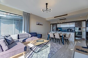 Een moderne woonkamer met een bank, een eettafel en een keuken met kasten en apparatuur.