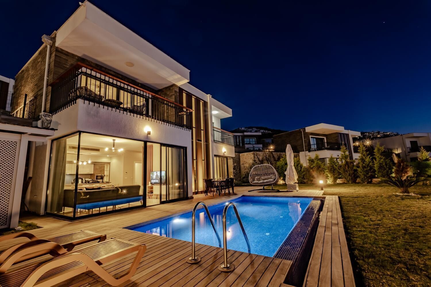 Ein modernes, zweistöckiges Haus mit Pool, Sitzgelegenheit im Freien und einem gut beleuchteten Balkon.