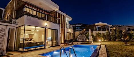 Ein modernes, zweistöckiges Haus mit Pool, Sitzgelegenheit im Freien und einem gut beleuchteten Balkon.