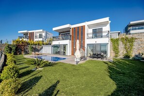Ett modernt hus i två våningar med en swimmingpool, en uteplats och en mur av sten.