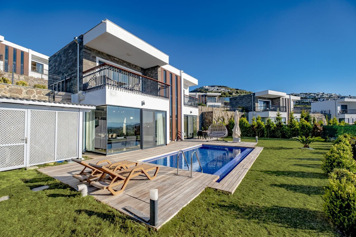 A modern two-story house with a swimming pool, a balcony, and a well-maintained garden.